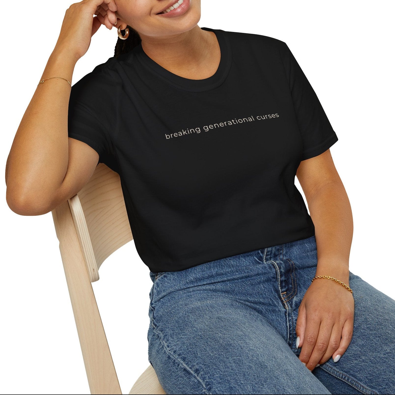 Woman wearing a black t-shirt with text, breaking generational curses sitting on a chair against a white background