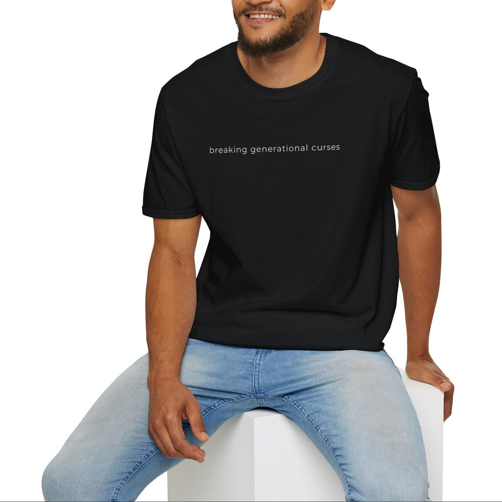 Man wearing a black t-shirt with text breaking generational curses sitting on a white stool against a white background.