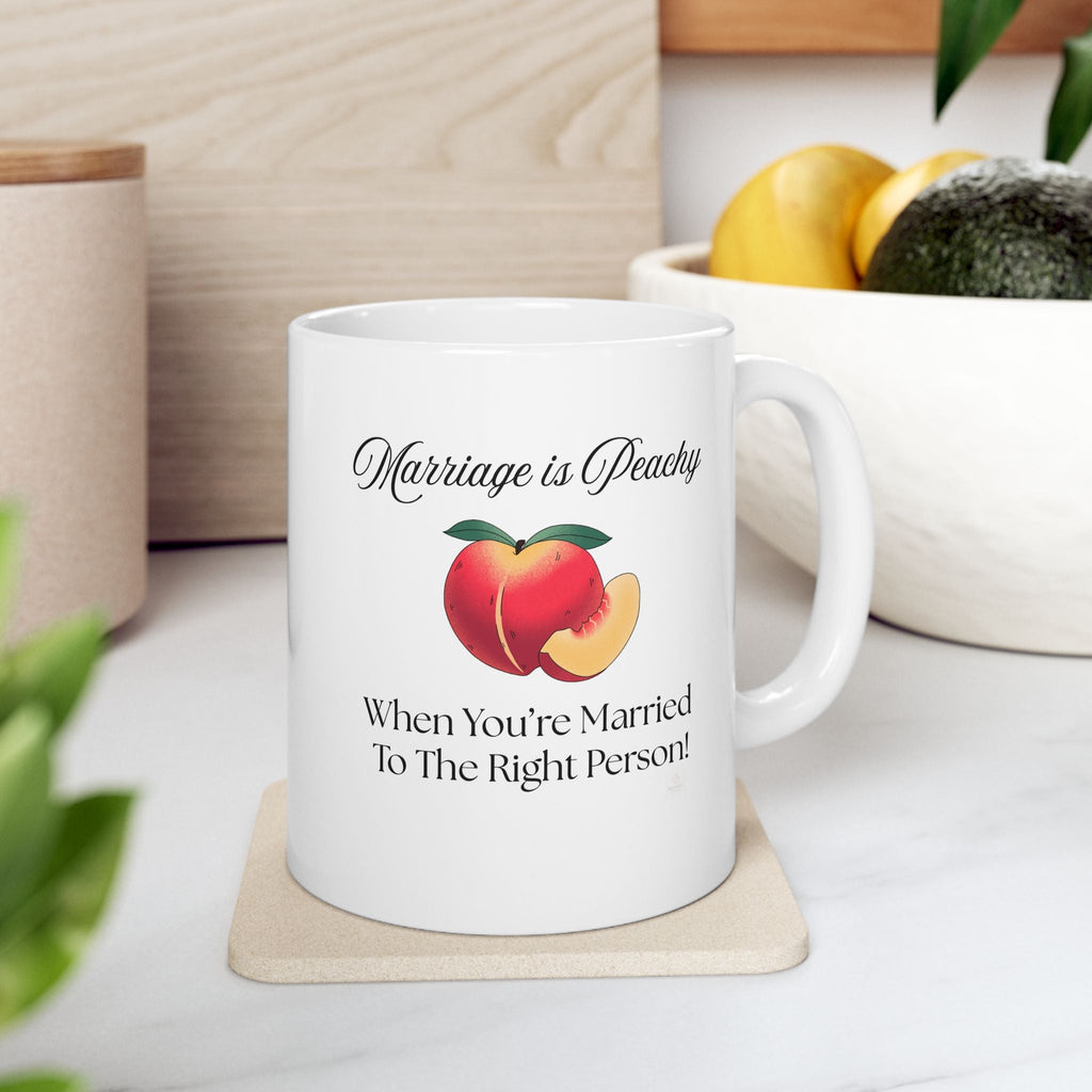 White ceramic love quote mug with peach design and text on a coaster, surrounded by fruits and plants.