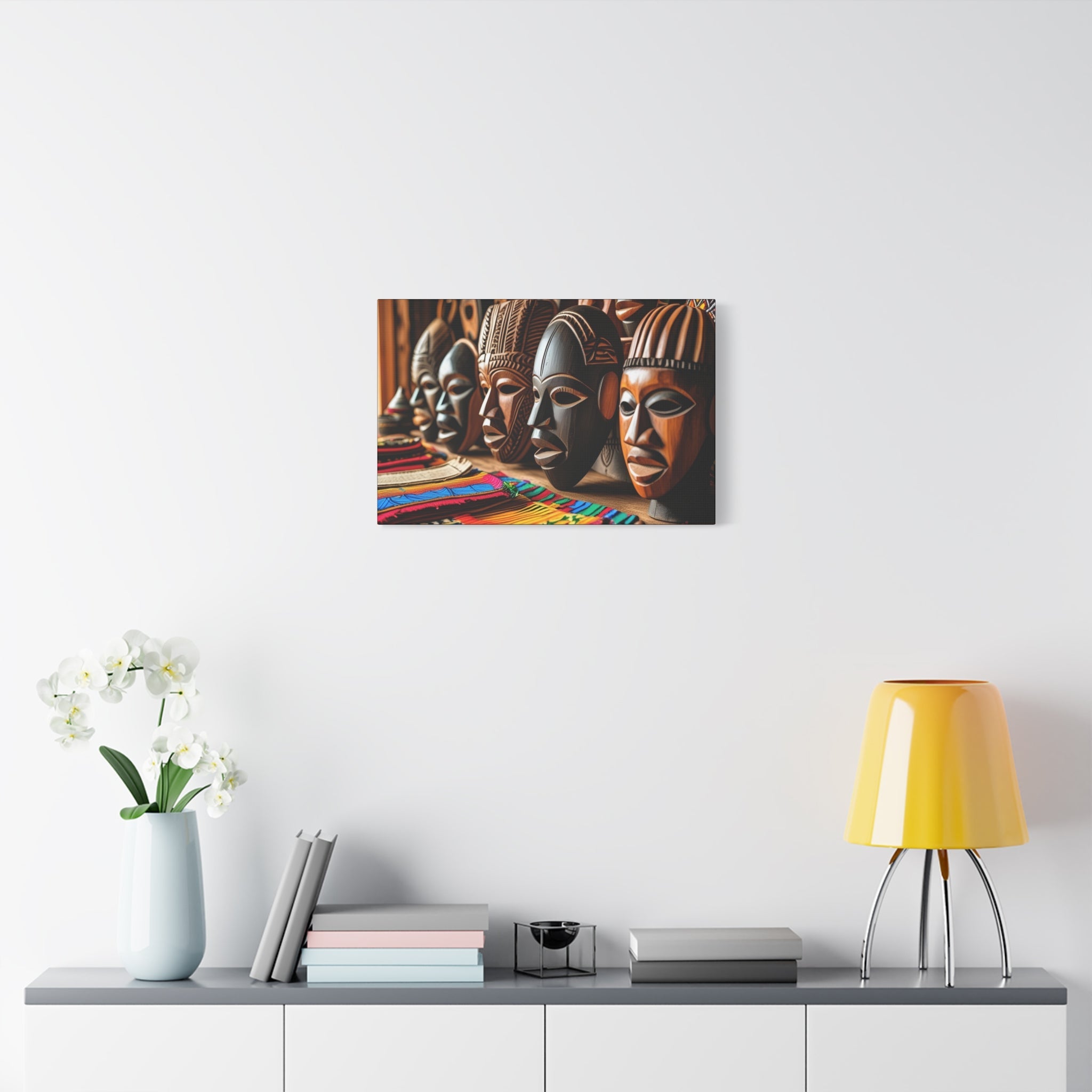 Decorative bohemian wall art of African masks on a white wall above a shelf with books and a lamp.