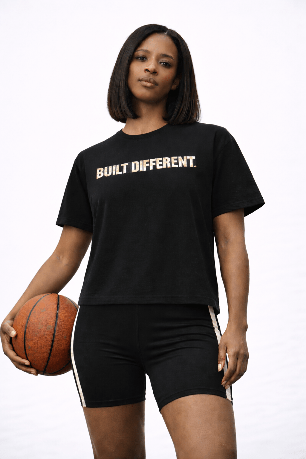 Woman wearing a black 'Built Different' t-shirt holding a basketball on a white background