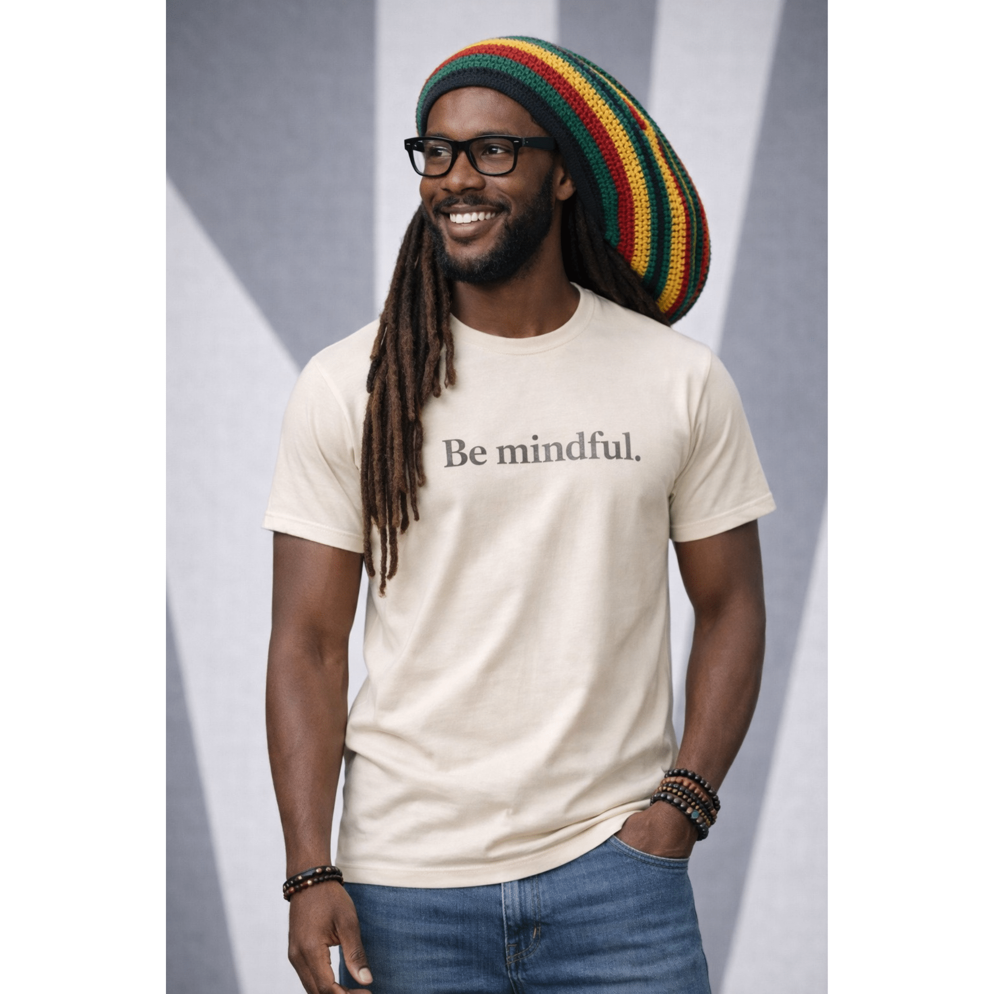 Man wearing a beige t-shirt with text 'Be mindful' with a colorful hat and glasses against a gray background