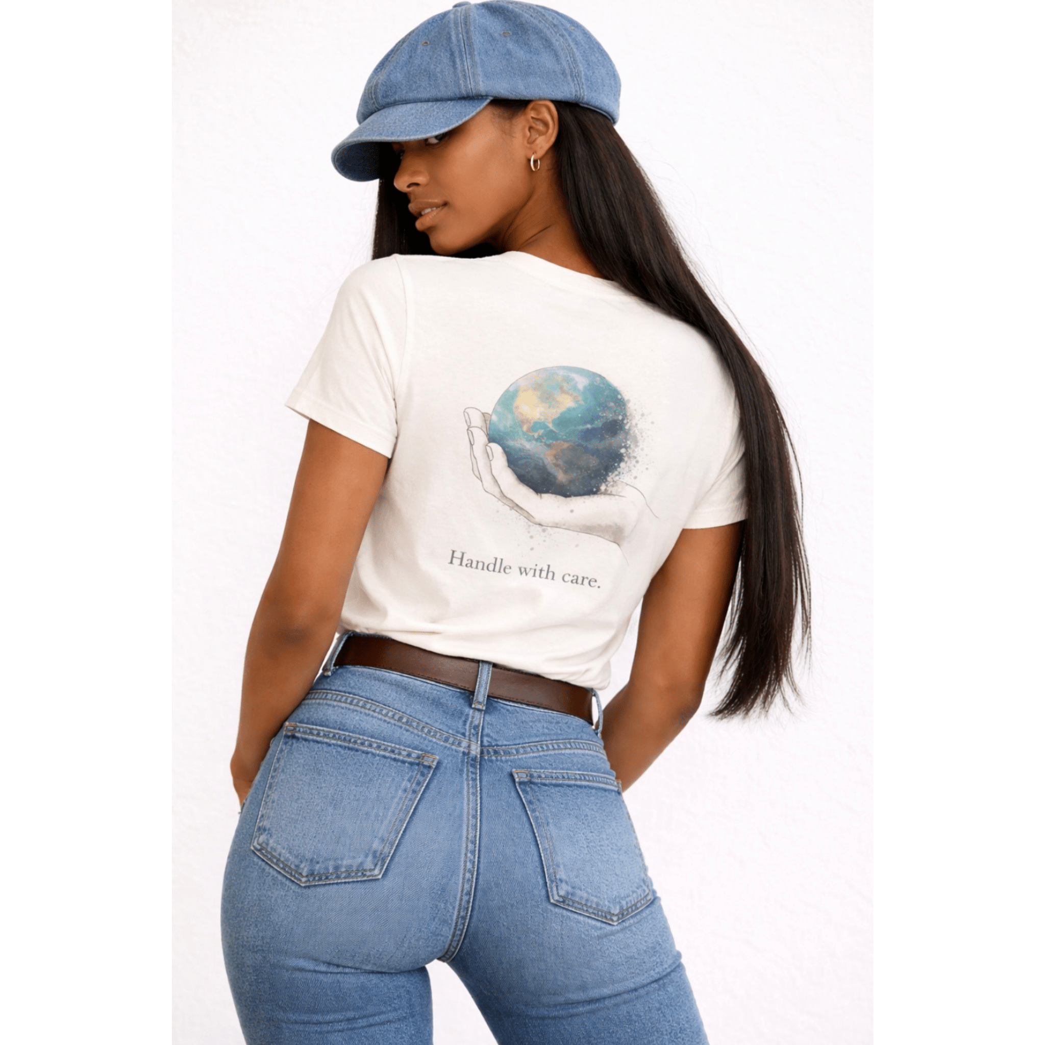 Person wearing back view of beige t-shirt with a graphic design of globe and text 'Handle With Care', paired with blue jeans and a denim cap.