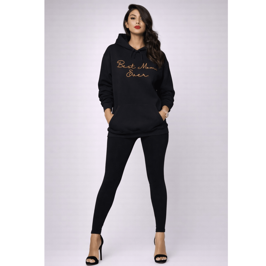 Woman wearing a black hoodie with 'Best Mom Ever' text with black leggings on a white background