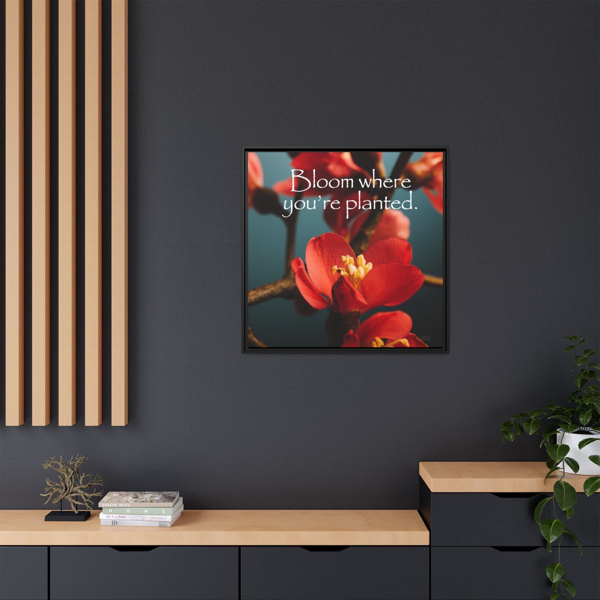 Framed artwork with red flowers and text on a dark wall above a wooden shelf.