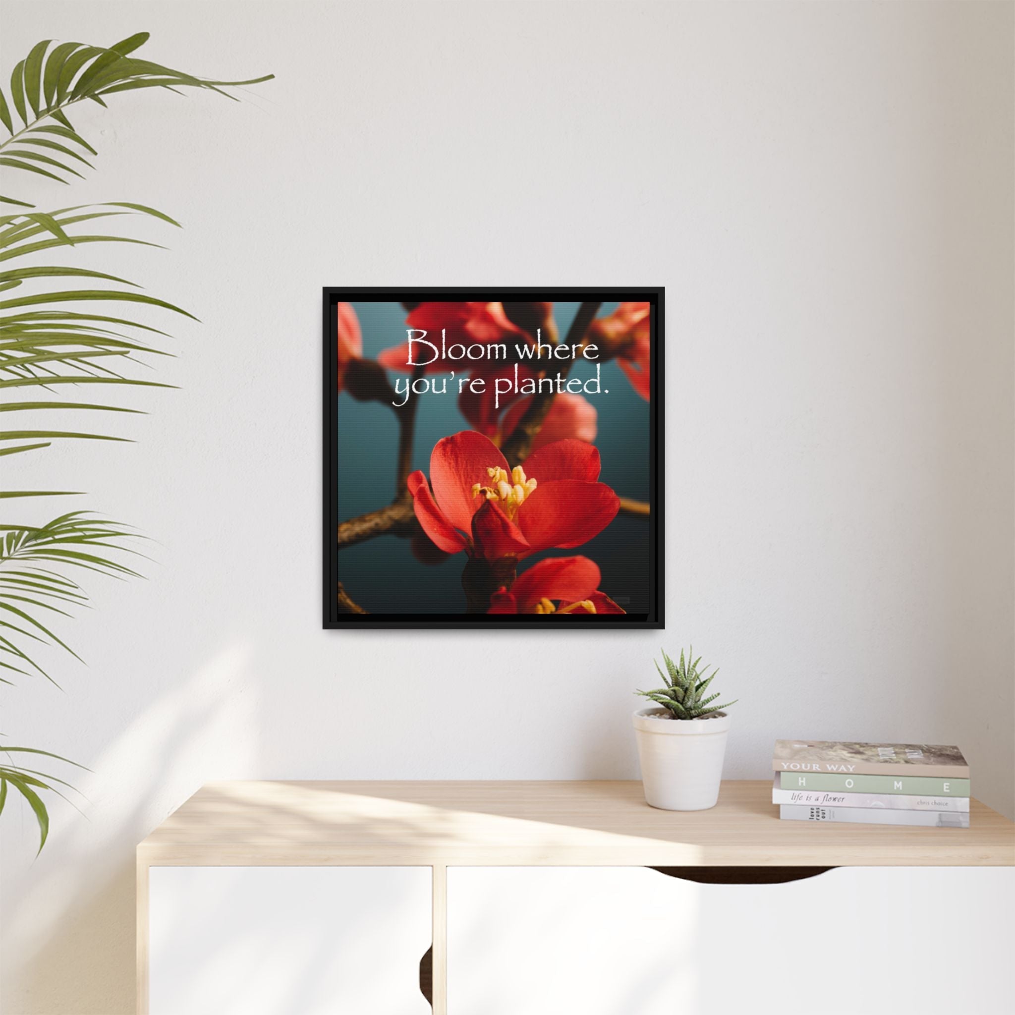Framed artwork with red flower and inspirational quote on a wall above a desk.