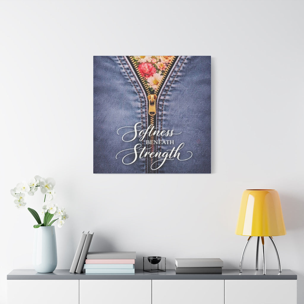 Wall art with floral zipper design and 'Softness Beneath Strength' text on a denim background, displayed in a room.