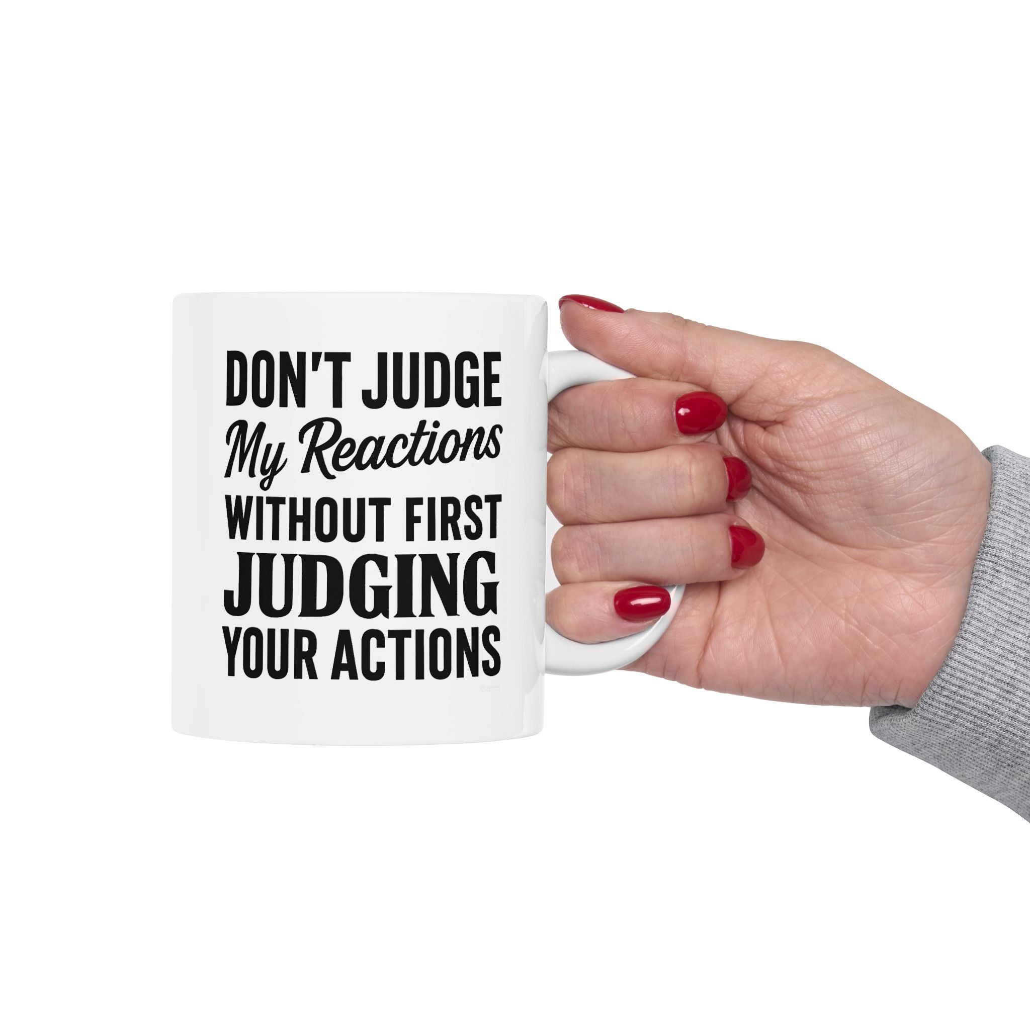 Hand holding a mug with text 'Don't judge my reactions without first judging your actions' on a white background