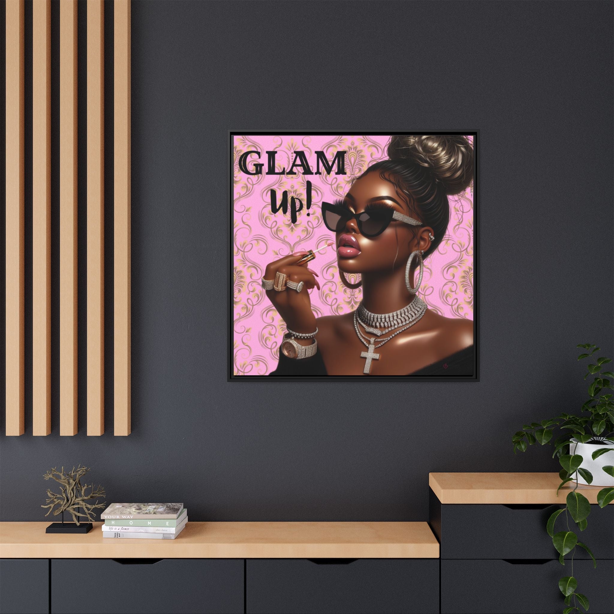 Framed artwork of a woman with 'GLAM up!' text on a pink background, displayed on a dark wall.