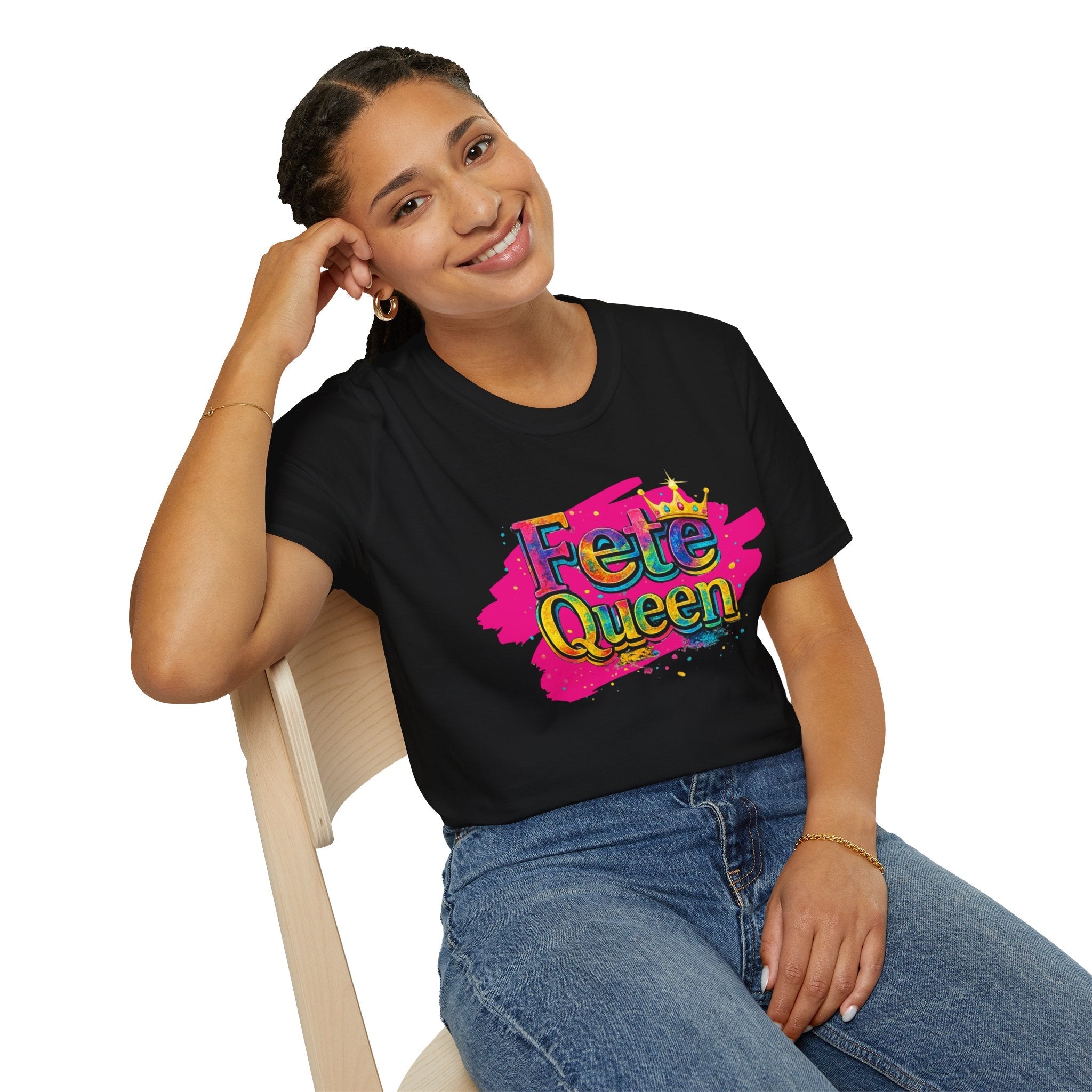 Woman wearing a black t-shirt with 'Fete Queen' colorful design, sitting on a chair.
