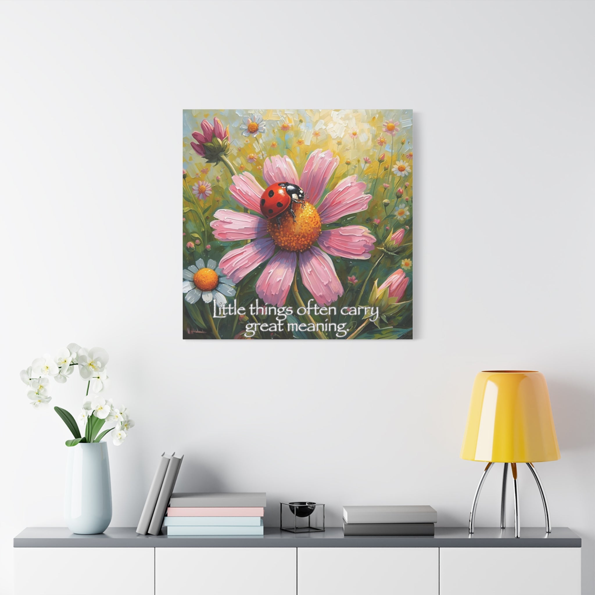 Canvas print of ladybug on a pink flower with a quote against bed of flowers, displayed on a wall above a shelf.