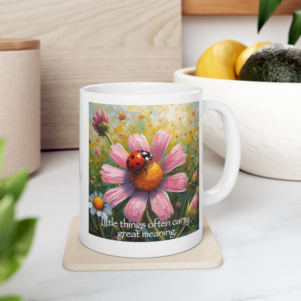 White mug with a floral design and text on a coaster, placed on a surface with fruit, plant, and container in the background.
