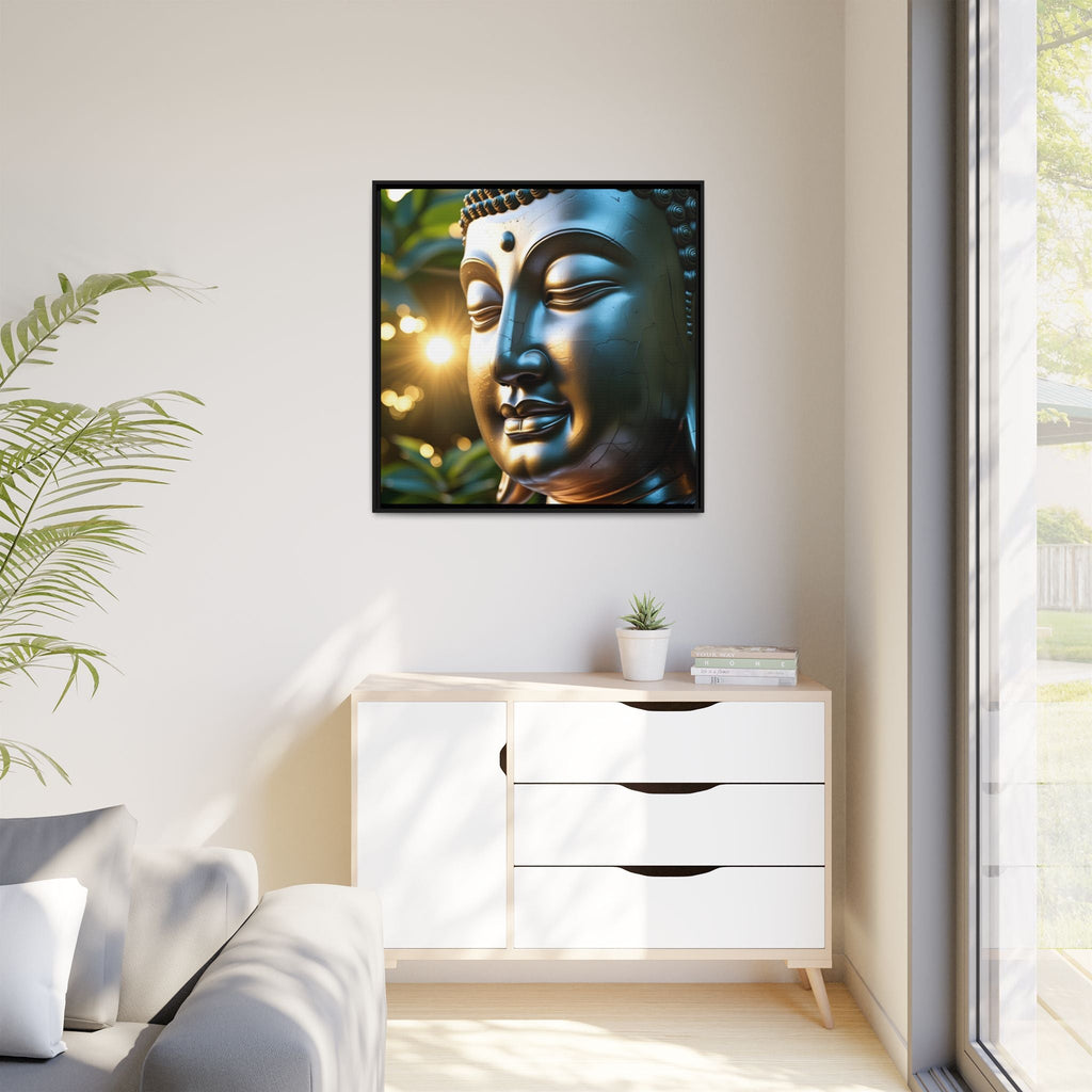 Framed art decor of a Buddha's face on a wall above a white cabinet with a plant and books next to window.