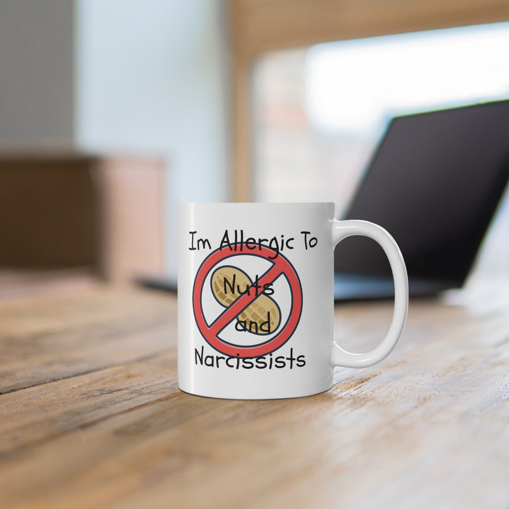 Mug with a humorous allergy-themed about nuts and narcissists design on a wooden surface.