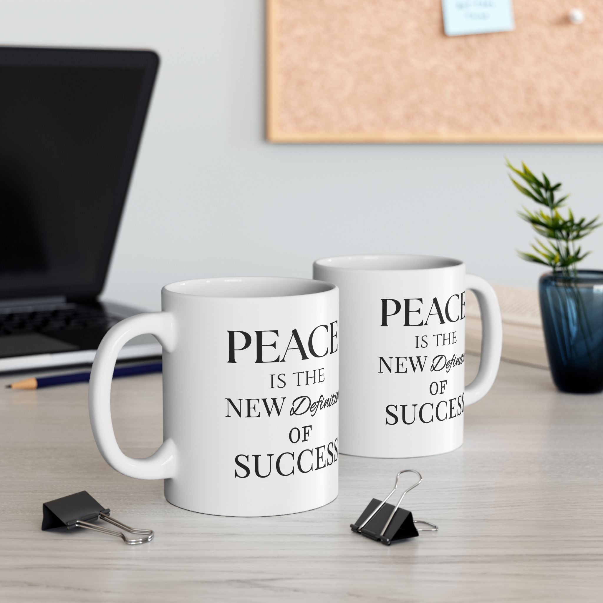 Two mugs with motivational quotes on a desk with office supplies.