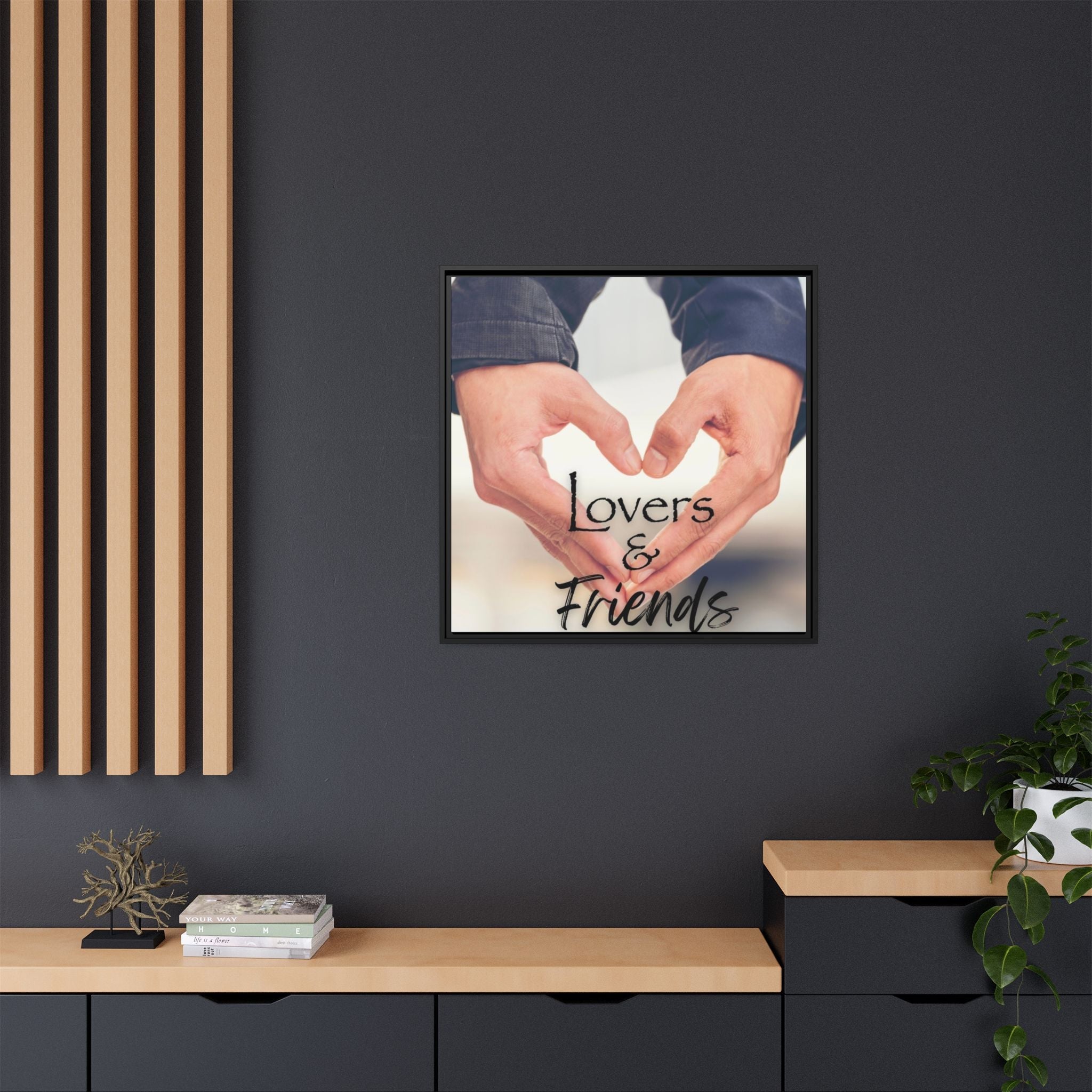 Framed artwork with two male hands forming a heart shape and 'Lovers & Friends' text on a dark wall.
