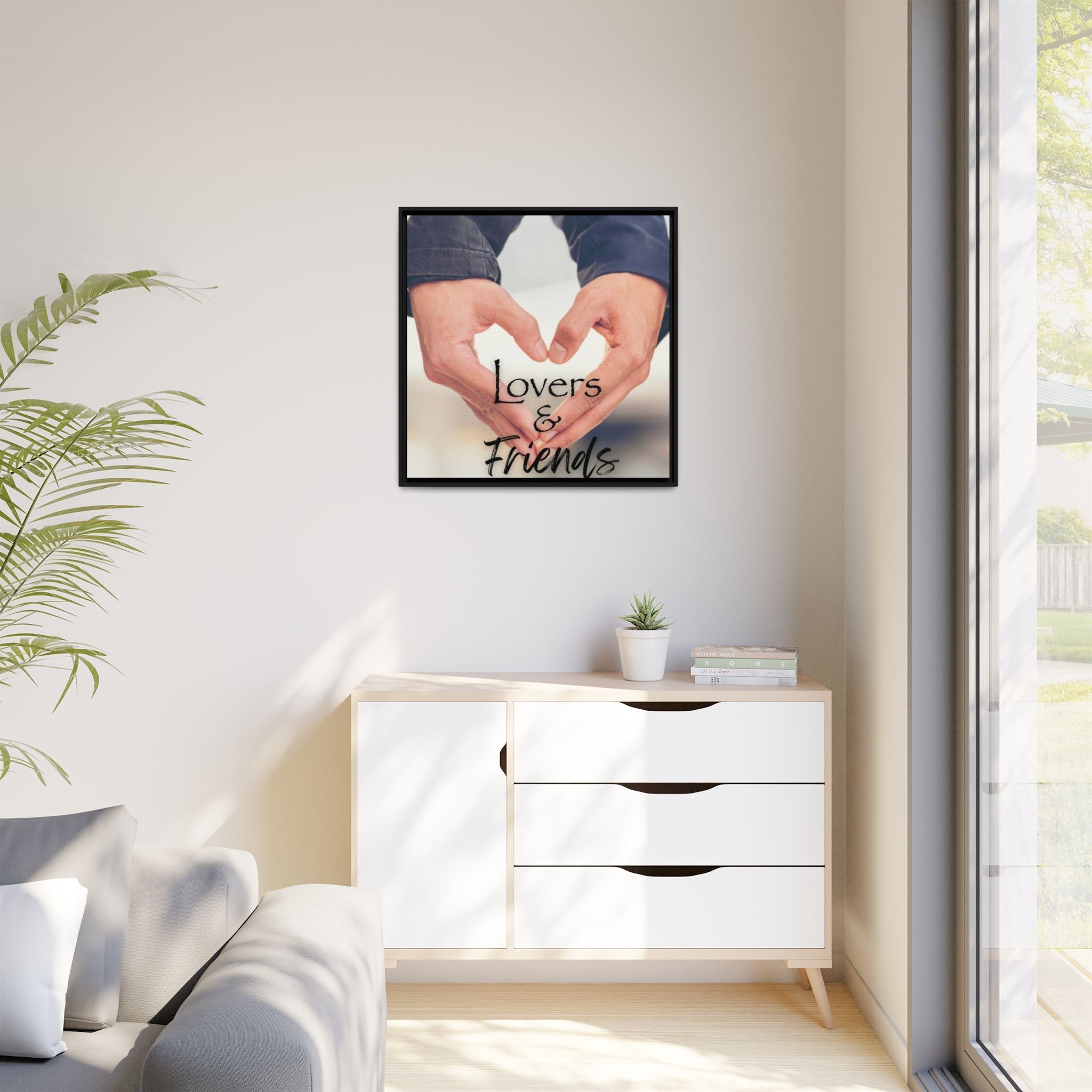 Framed artwork with hands forming a heart shape on a wall above a white cabinet in living room.