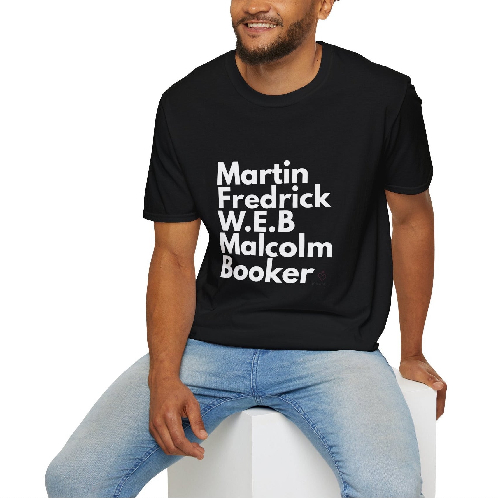 Man wearing a black t-shirt with text of black leaders sitting on a white stool against a white background