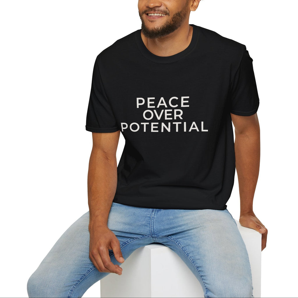 Man wearing a black t-shirt with 'PEACE OVER POTENTIAL' text, sitting on a white stool against a white background.