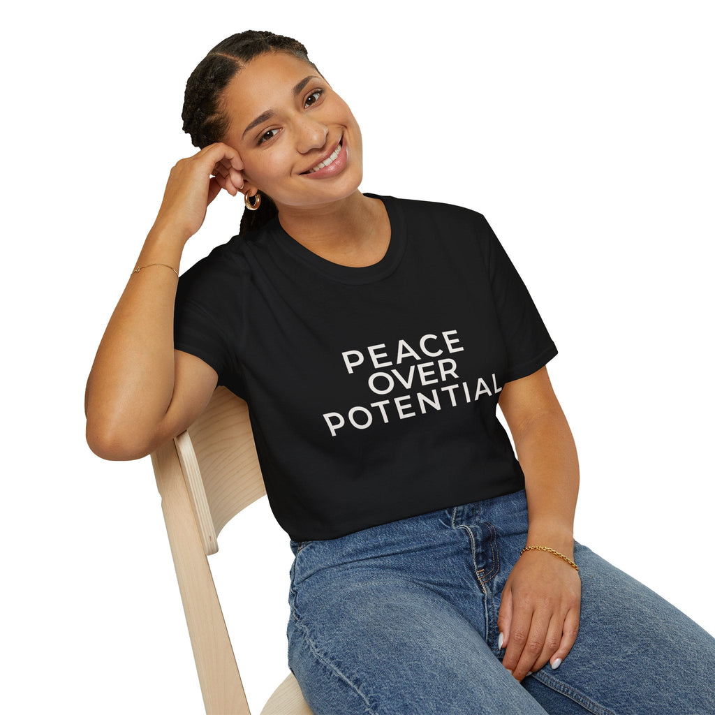Woman wearing a black t-shirt with 'PEACE OVER POTENTIAL' text, sitting on a chair.