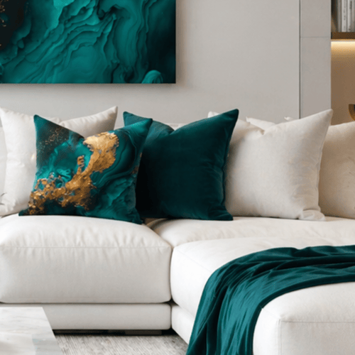 Beige sofa with decorative abstract emerald and gold pillows and a teal blanket in a living room setting.