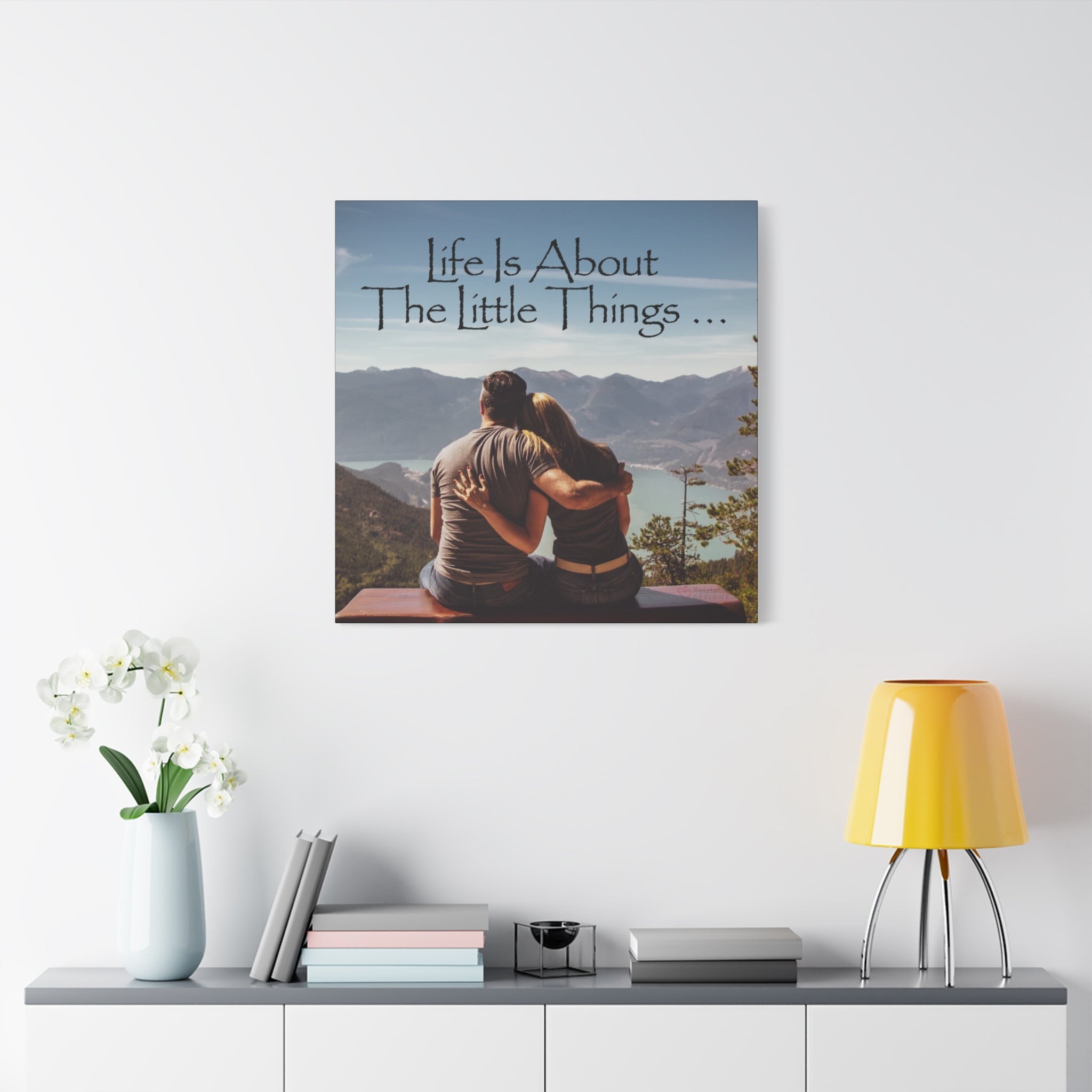 Canvas print with a couple sitting together and 'Life is About The Little Things' text, displayed on a wall above a shelf.