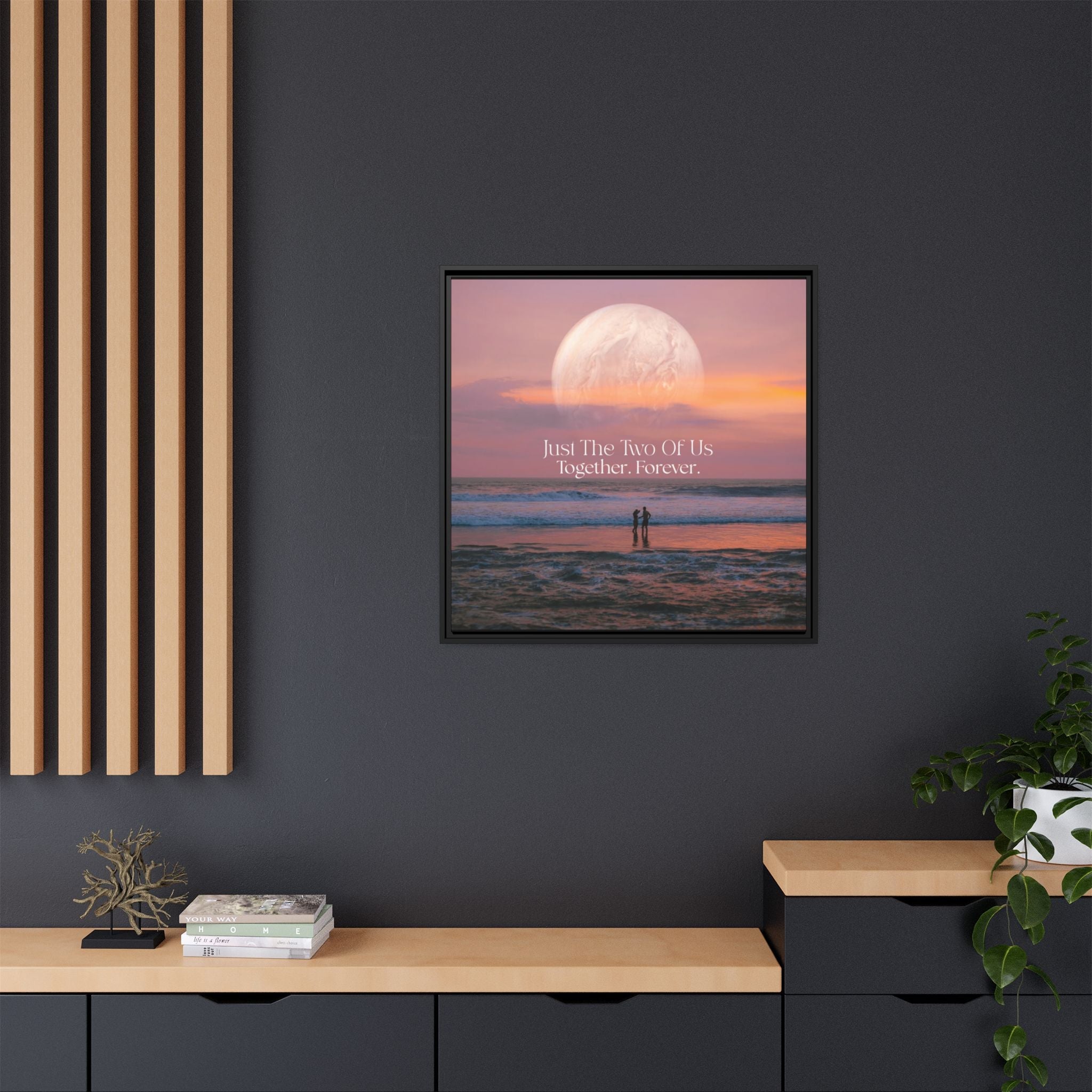 Framed romantic artwork with a couple on a beach under a full moon, displayed on a dark wall.