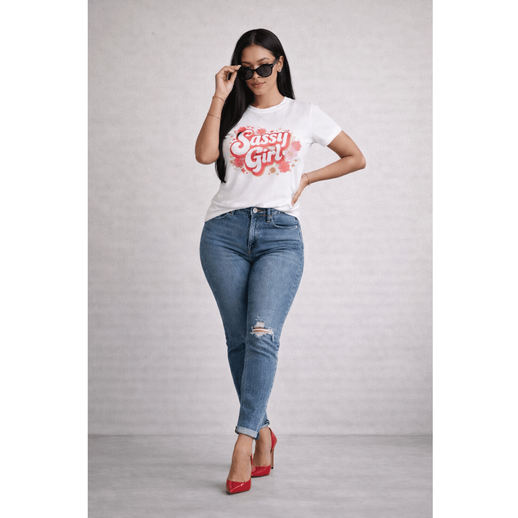 Woman wearing a 'Sassy Girl' t-shirt, blue jeans, sunglasses and red shoes on a plain background