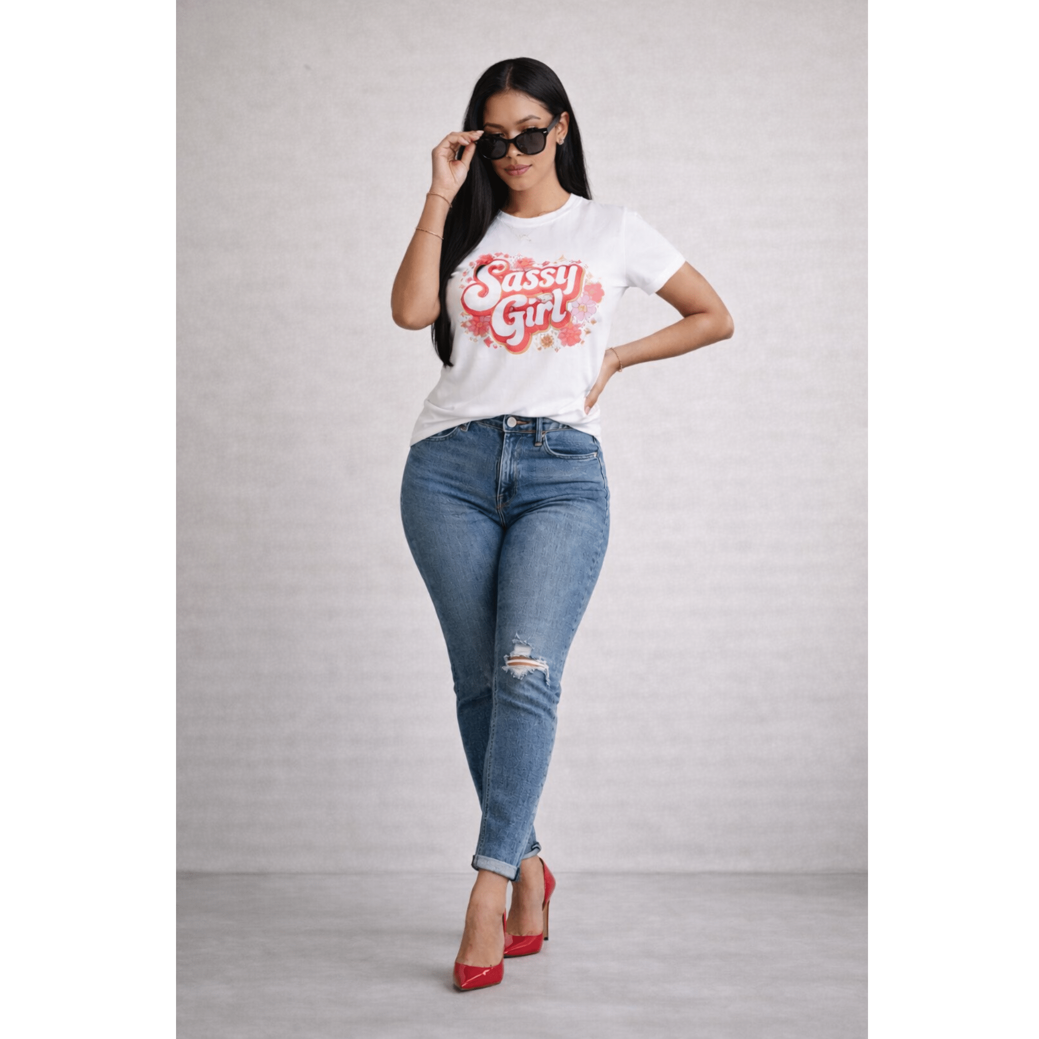 Woman wearing a 'Sassy Girl' t-shirt, blue jeans, sunglasses and red shoes on a plain background