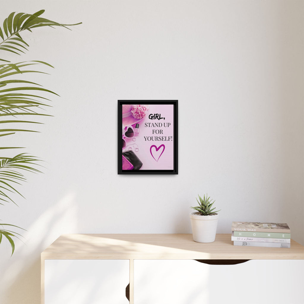 Framed motivational girl power print on a wall above a desk with a plant and books.