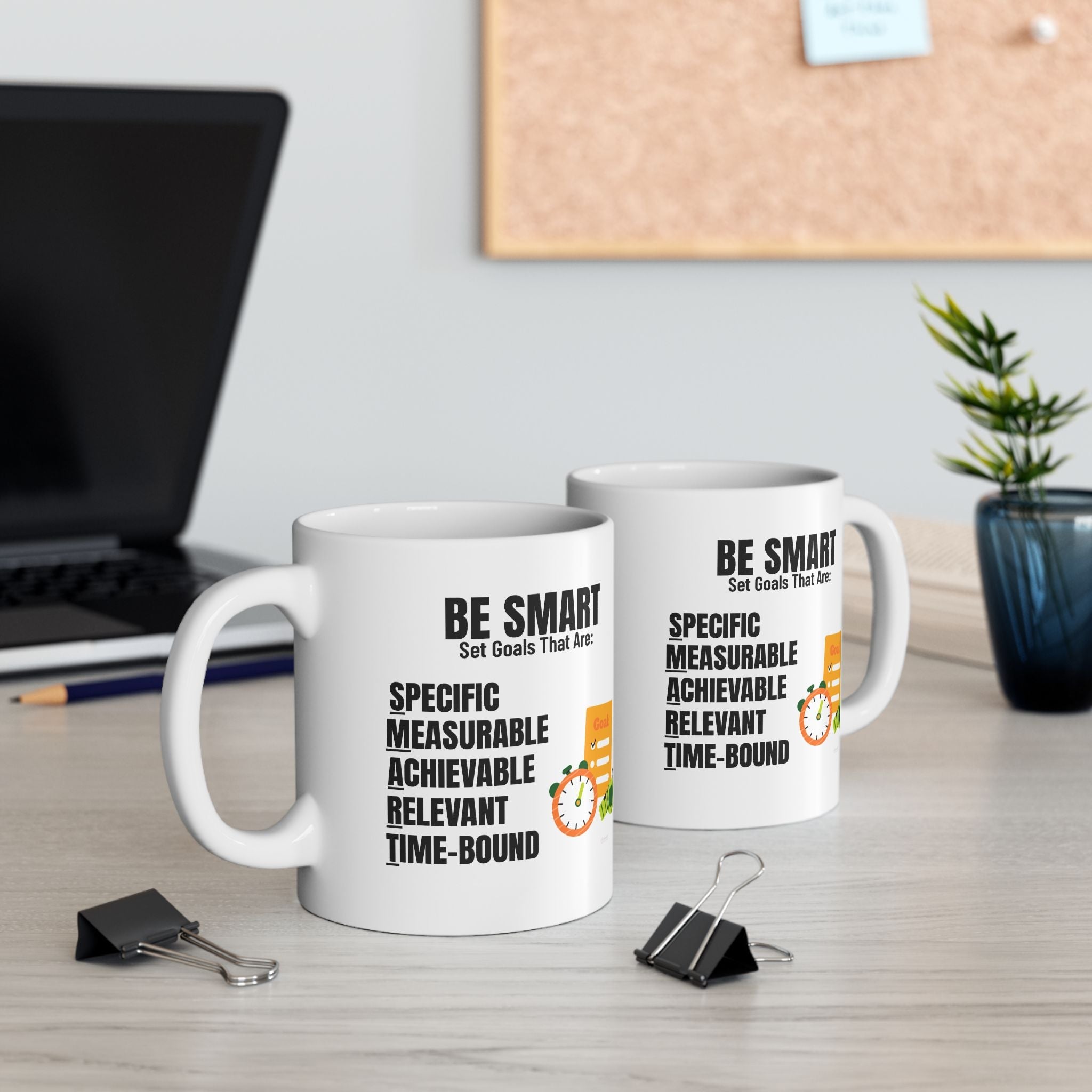 Two white SMART GOALS mugs with motivational text on a desk with office supplies and decor.