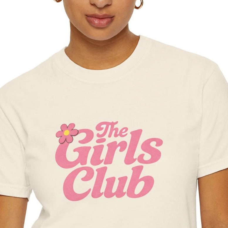 Woman wearing an ivory t-shirt with 'The Girls Club' in pink text and a flower graphic.