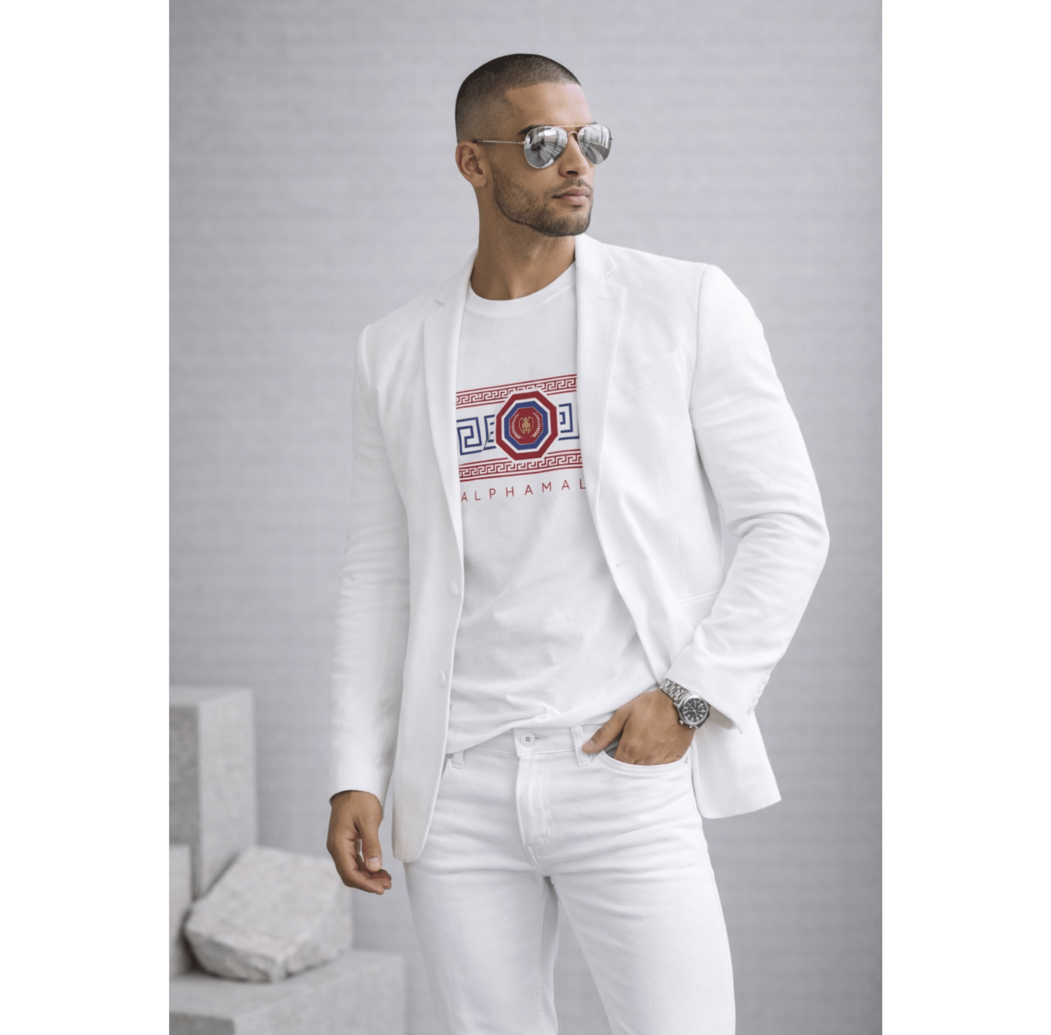 Man wearing a white blazer with a white tee a red and blue geometric logo and white pants on a gray background